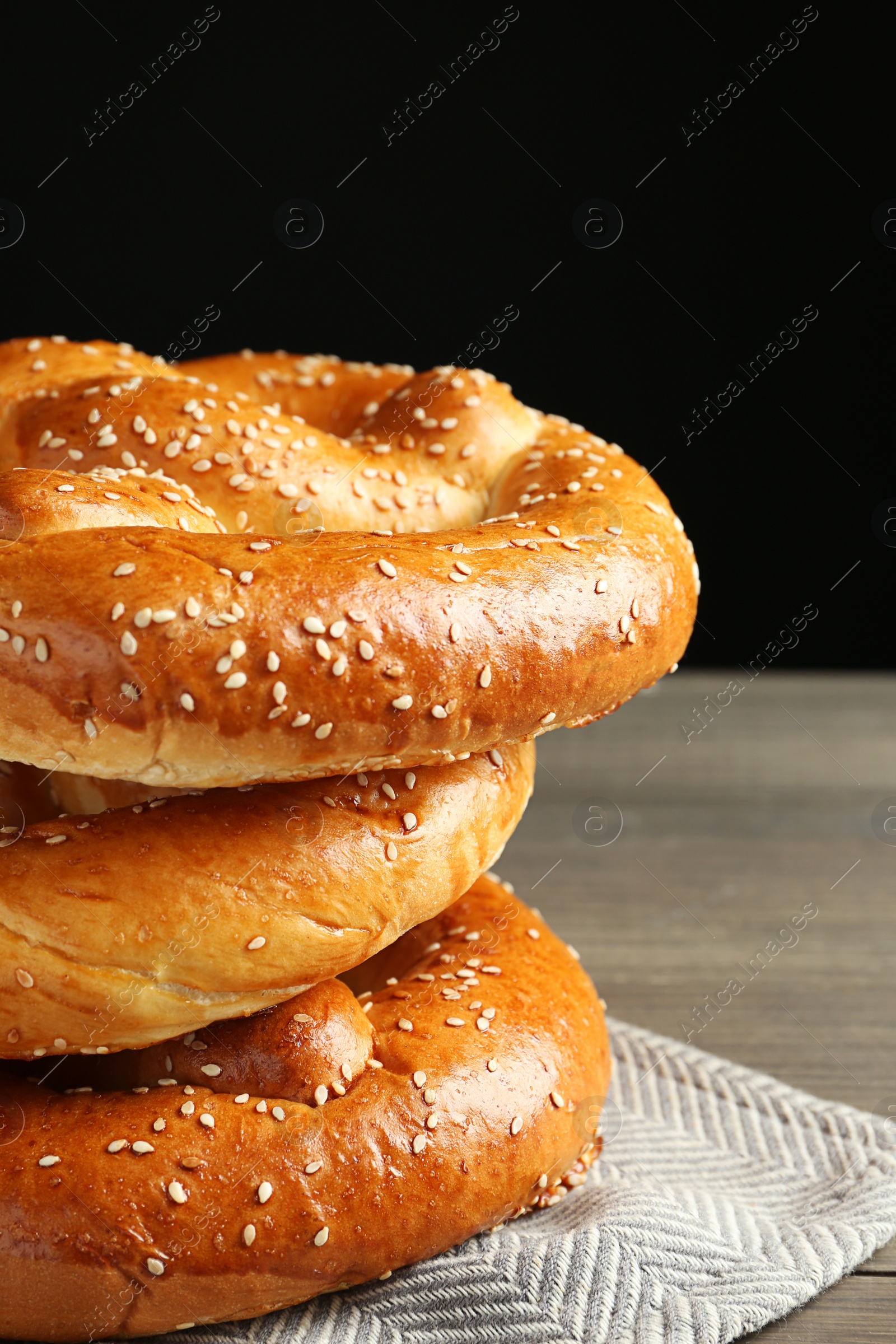 Photo of Tasty freshly baked pretzels on wooden table against black background, closeup