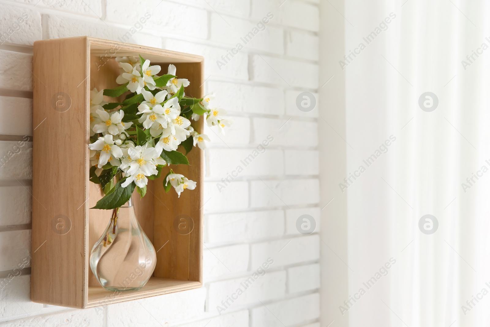 Photo of Wooden shelf with bouquet of beautiful jasmine flowers in vase on white brick wall, space for text