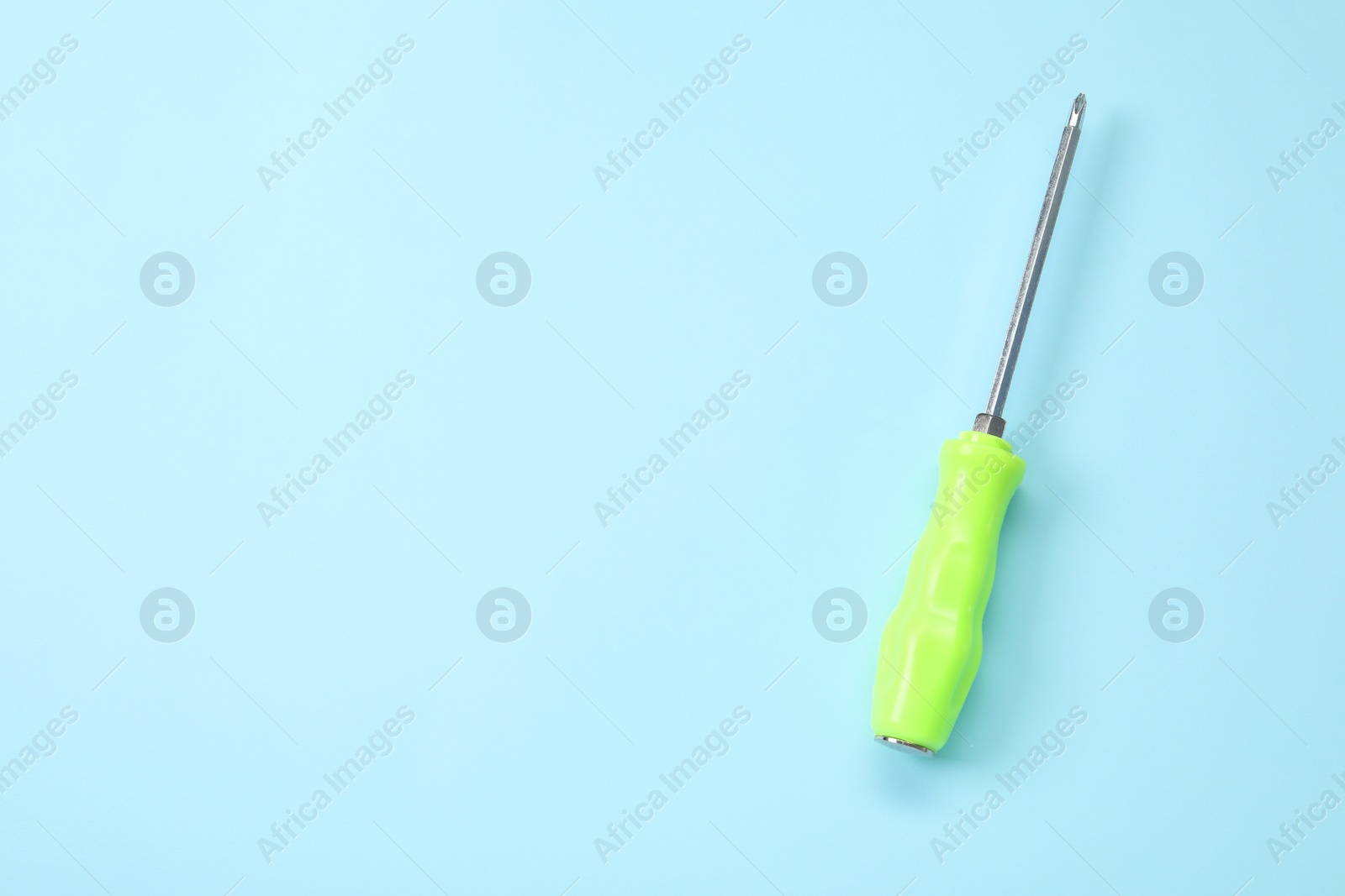 Photo of Screwdriver with green handle on light blue background, top view. Space for text