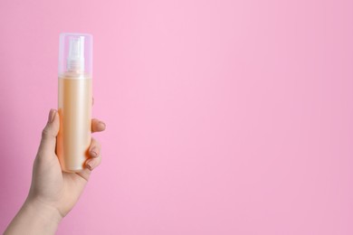 Woman holding spray bottle with thermal protection on light pink background, closeup. Space for text