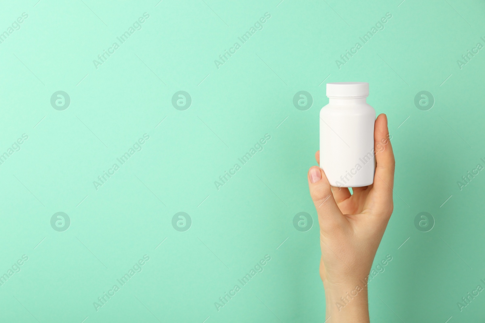 Photo of Woman holding blank white jar of vitamins on turquoise background, closeup. Space for text