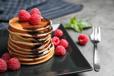 Photo of Delicious pancakes with fresh raspberries and chocolate syrup on grey table