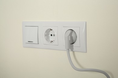 Photo of Power sockets with inserted plug and light switch on white wall indoors