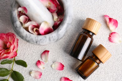 Photo of Glass bottles of aromatic essential oil, mortar with roses on white table, flat lay