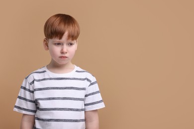 Portrait of sad little boy on beige background, space for text