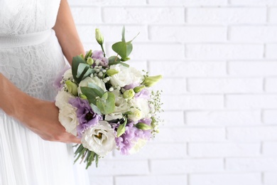 Photo of Bride holding beautiful bouquet with Eustoma flowers near brick wall, closeup. Space for text