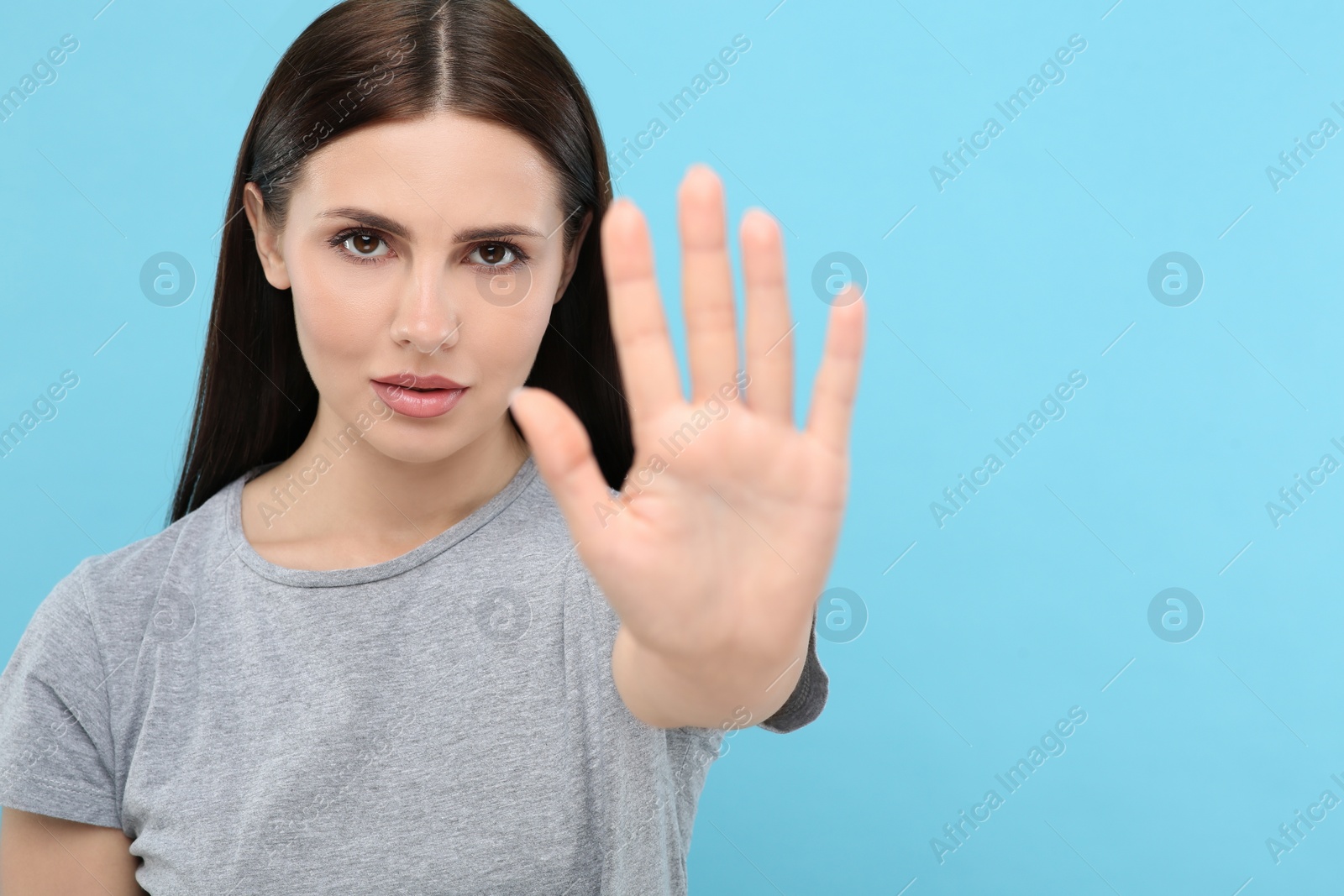 Photo of Woman showing stop gesture on light blue background, selective focus. Space for text