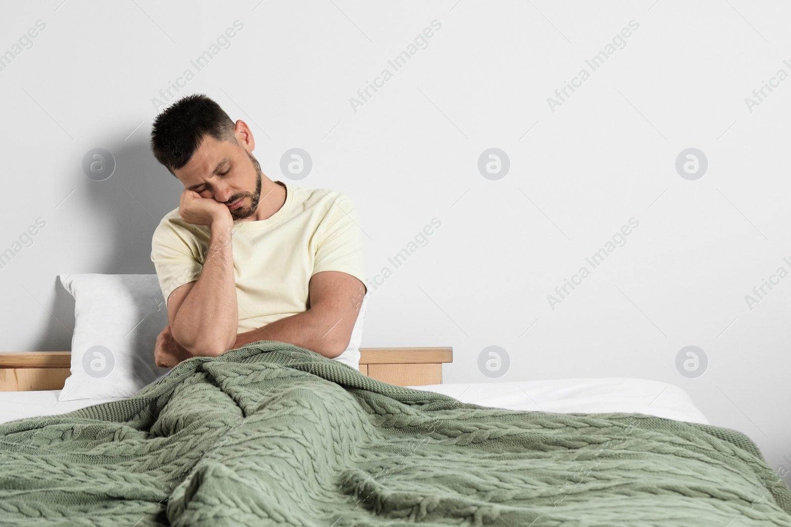 Photo of Sleep deprived man sitting on bed at home. Space for text