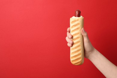 Photo of Woman holding delicious french hot dog on red background, closeup. Space for text