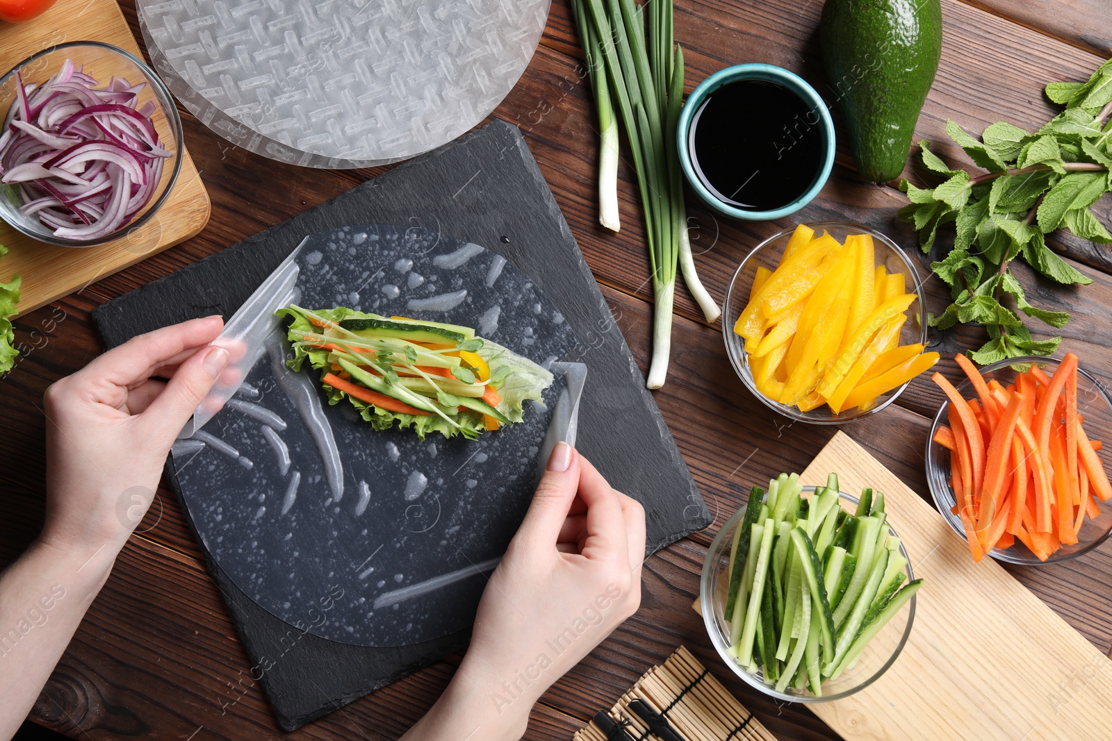 Photo of Woman making spring roll at wooden table with products, top view