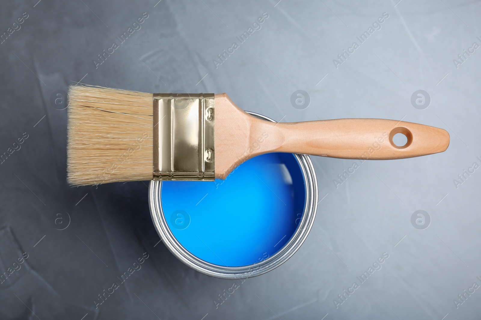 Photo of Can with blue paint and brush on gray background, top view