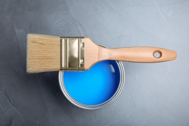 Photo of Can with blue paint and brush on gray background, top view
