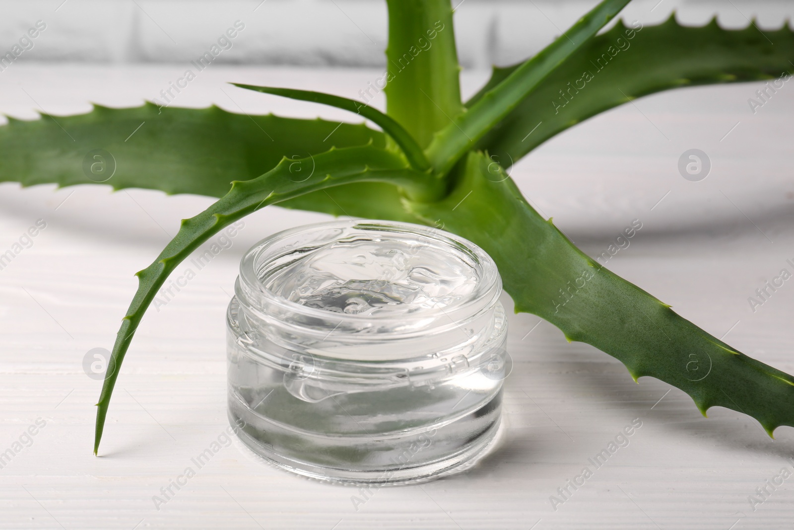 Photo of Jar of cosmetic gel and aloe vera leaves on white wooden table, closeup