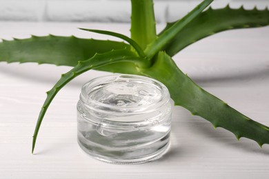 Jar of cosmetic gel and aloe vera leaves on white wooden table, closeup