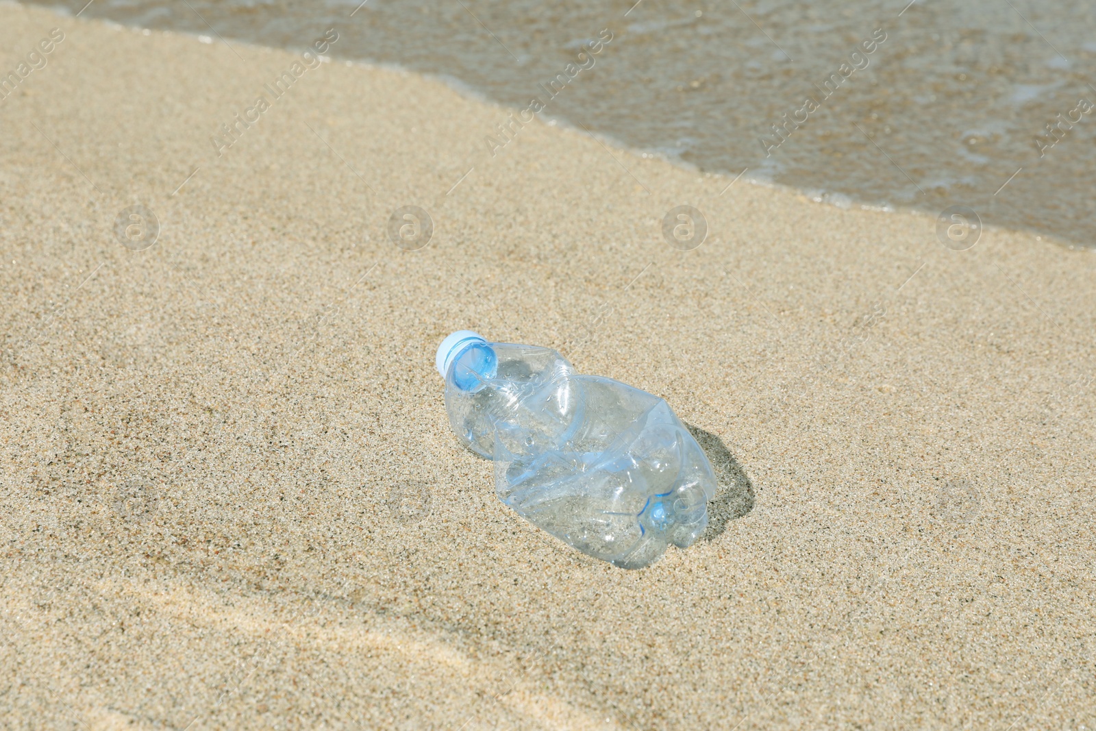 Photo of Used plastic bottle on sand near water. Recycling problem