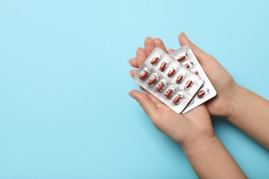 Photo of Woman holding blisters with pills on turquoise background, top view and space for text. Anemia treatment