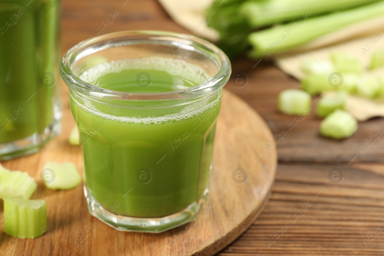 Photo of Glass of celery juice and fresh vegetables on wooden table, closeup