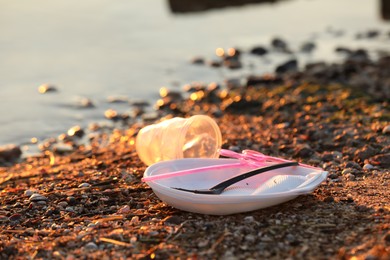 Photo of Used plastic tableware near water at beach, closeup and space for text. Environmental pollution concept