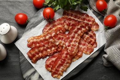 Photo of Fried bacon slices, tomatoes, parsley and spices on grey textured table, flat lay