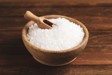 Photo of Bowl with natural sea salt and scoop on wooden table