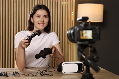 Photo of Smiling technology blogger with game controllers recording video review at home