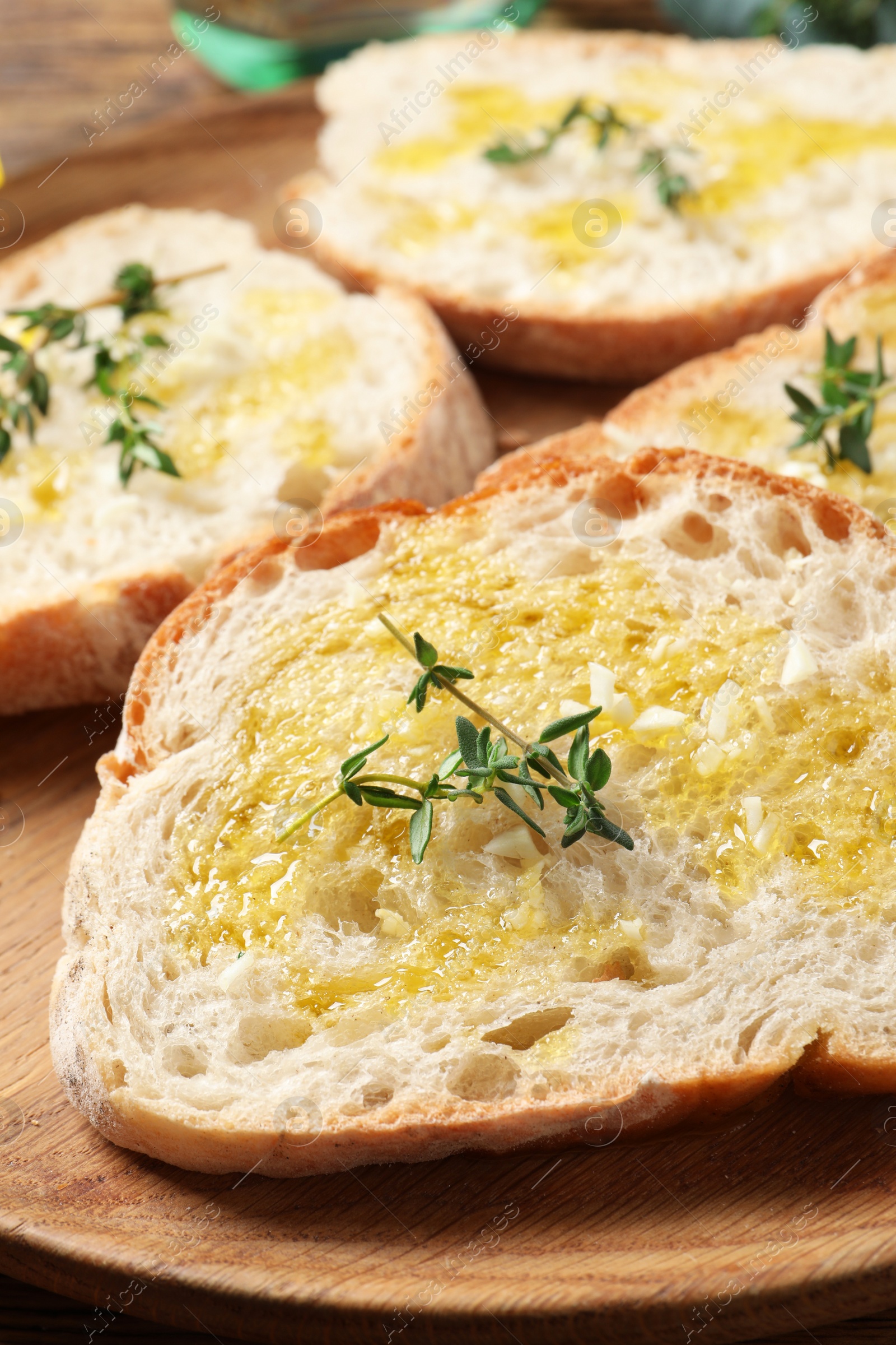 Photo of Tasty bruschettas with oil and thyme on wooden plate, closeup