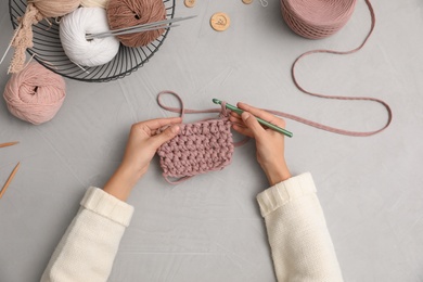 Photo of Woman crocheting with threads at grey table, top view. Engaging hobby