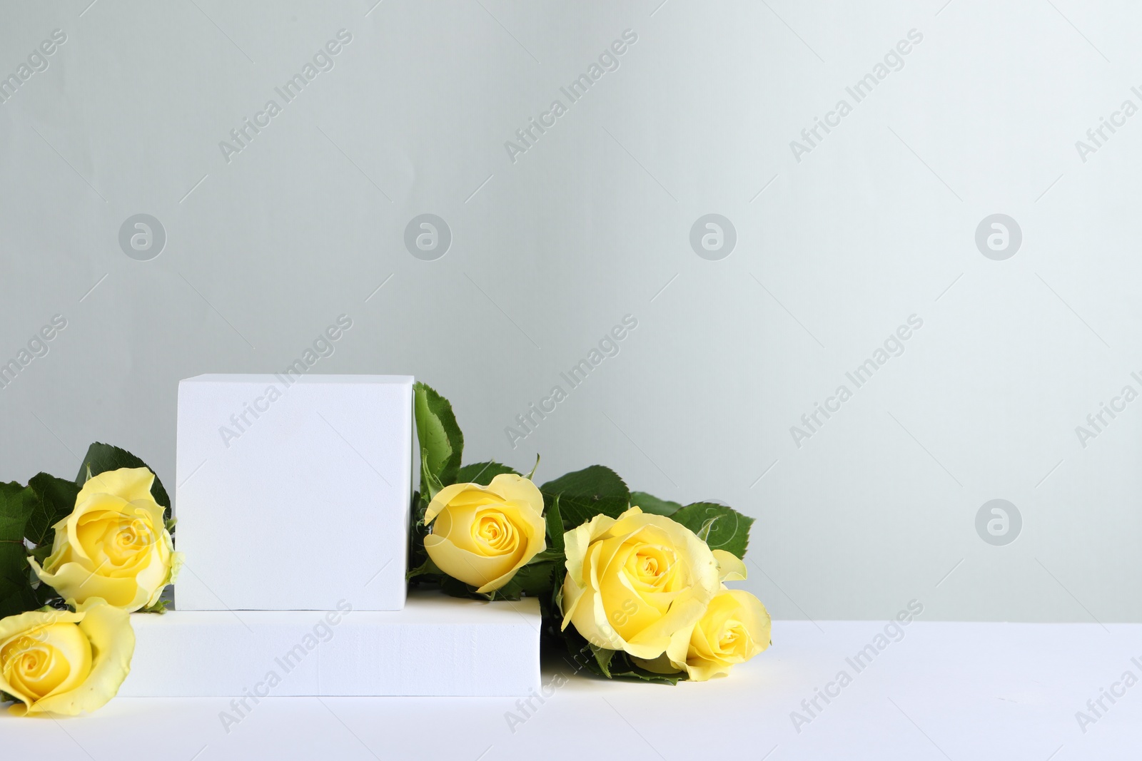 Photo of Beautiful presentation for product. Geometric figures and yellow roses on white table against light grey background, space for text