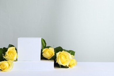 Photo of Beautiful presentation for product. Geometric figures and yellow roses on white table against light grey background, space for text
