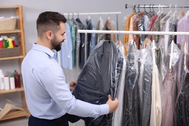 Dry-cleaning service. Worker taking jacket from rack indoors