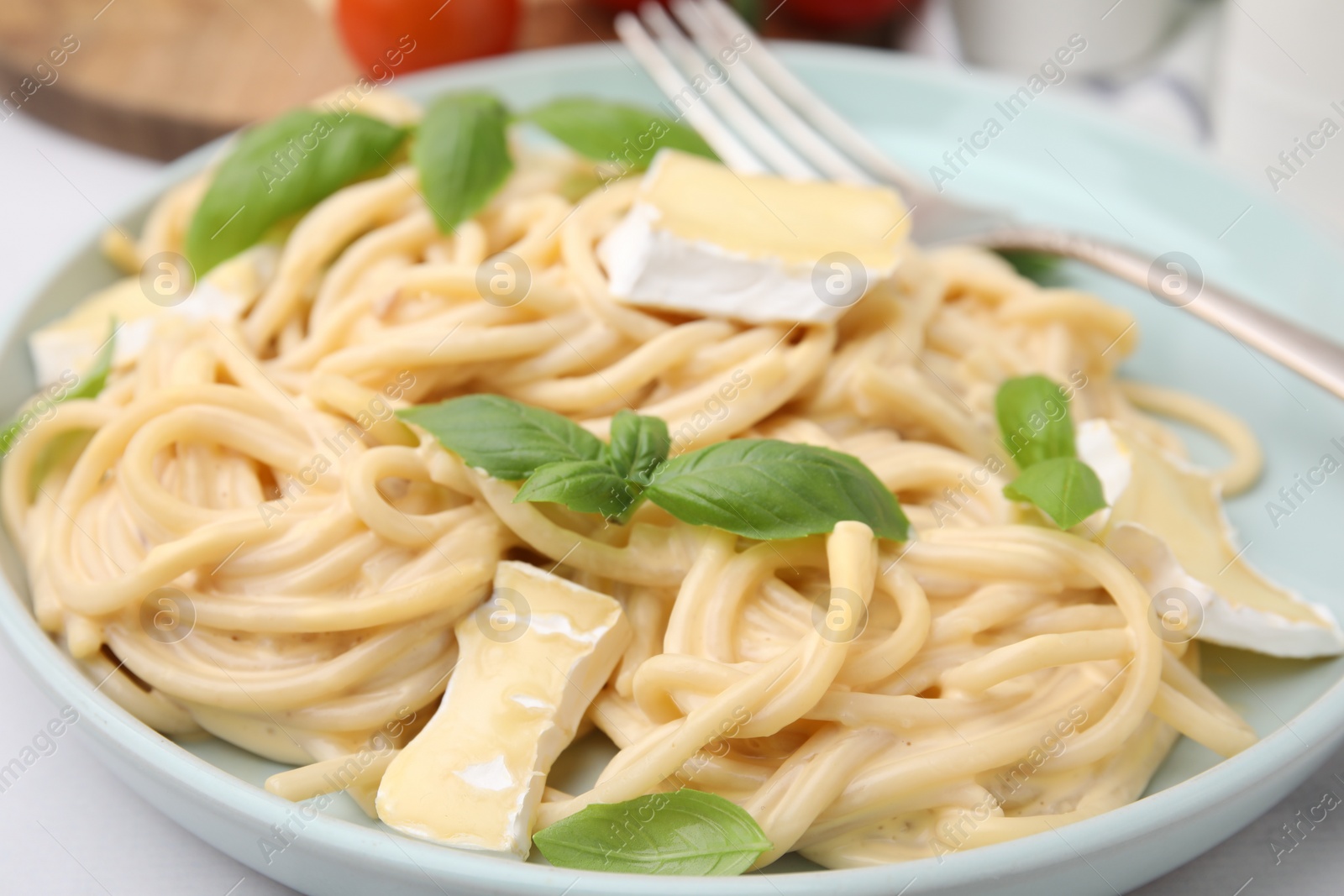 Photo of Delicious pasta with brie cheese and basil leaves on table, closeup