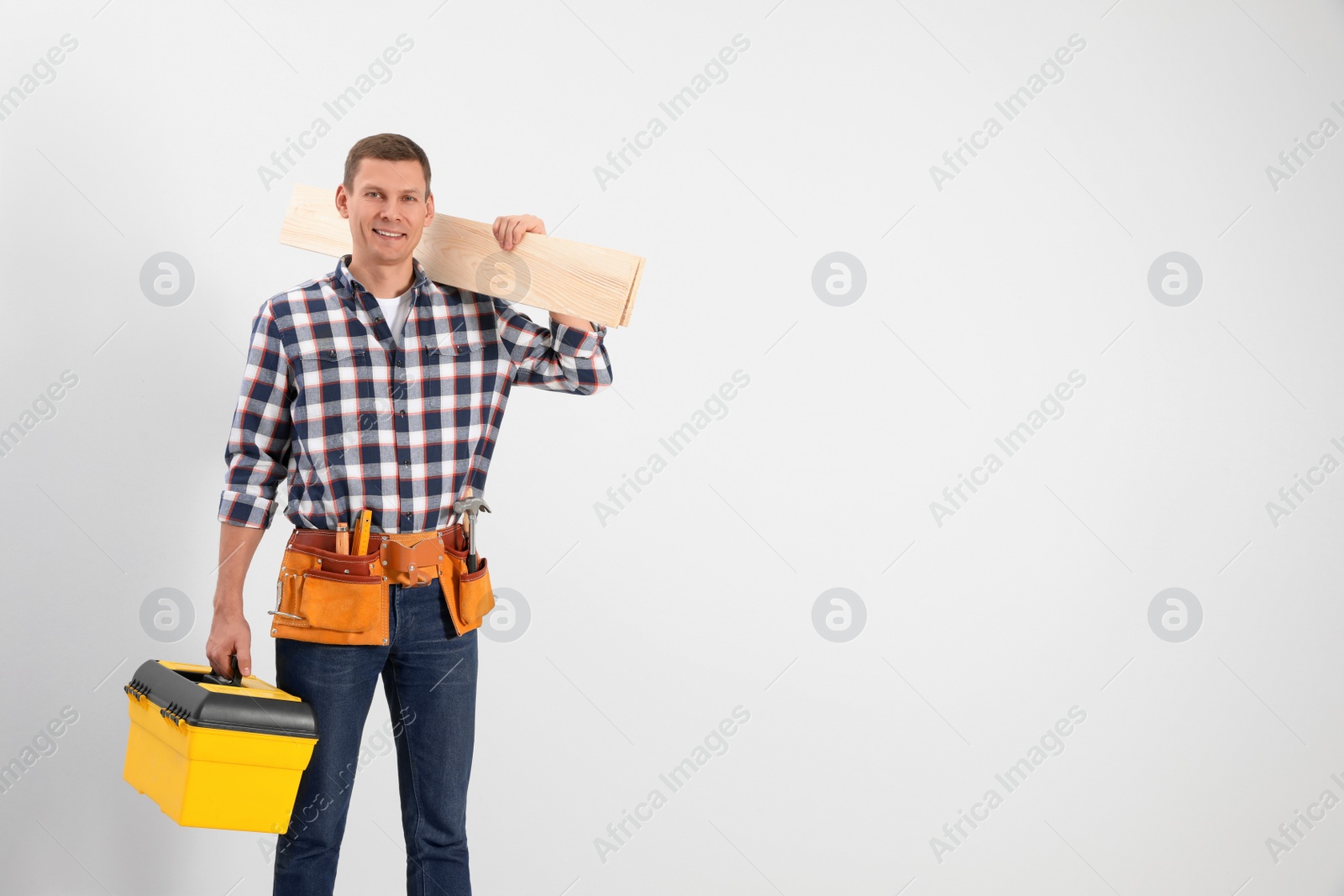 Photo of Handsome carpenter with wooden planks on light background. Space for text