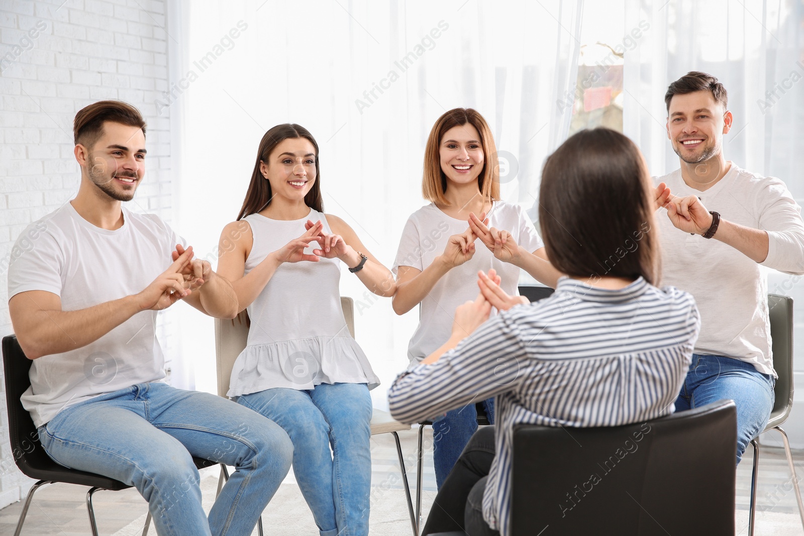 Photo of Group of young people learning sign language with teacher indoors