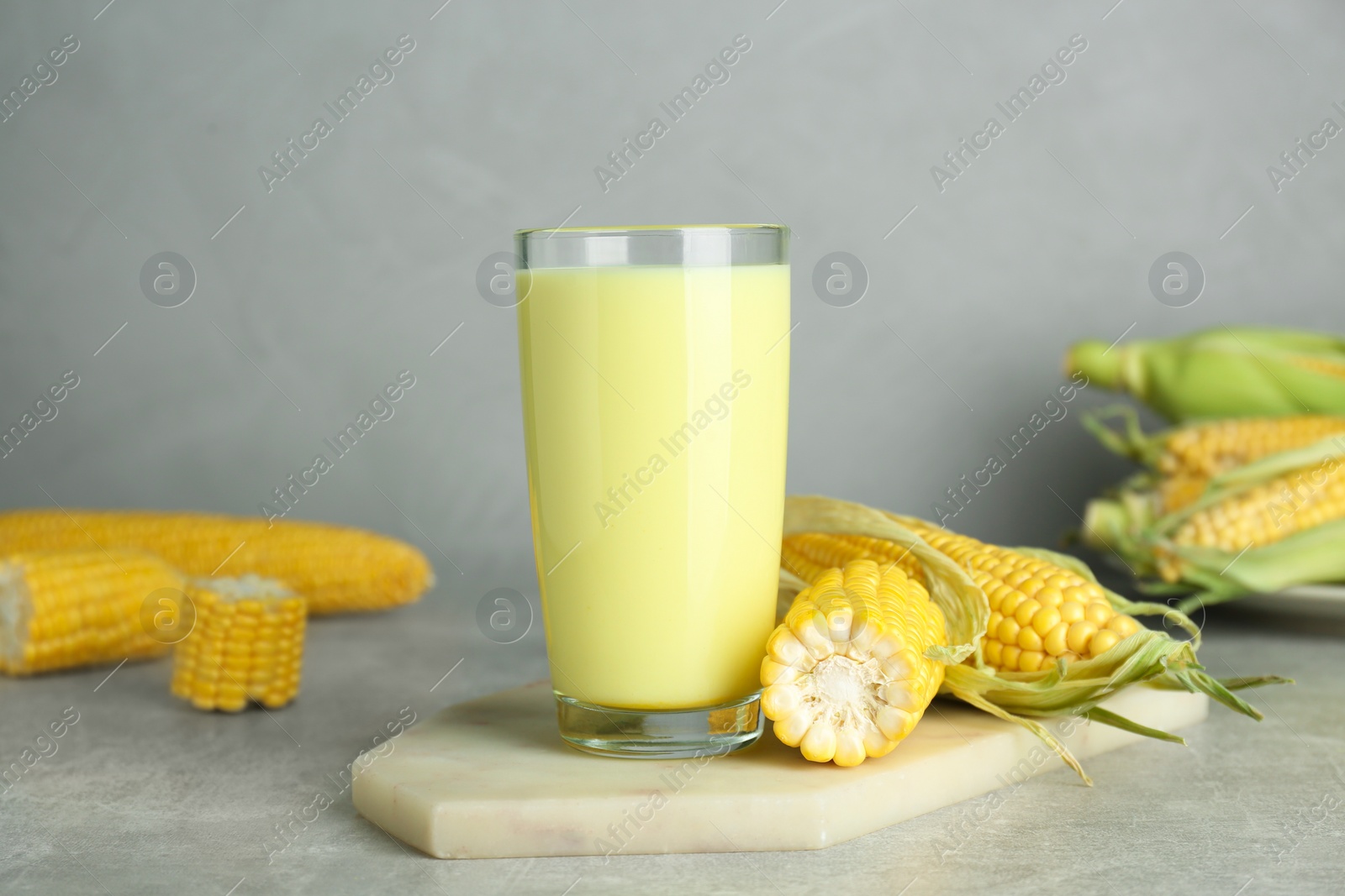 Photo of Tasty fresh corn milk in glass and cobs on light grey table