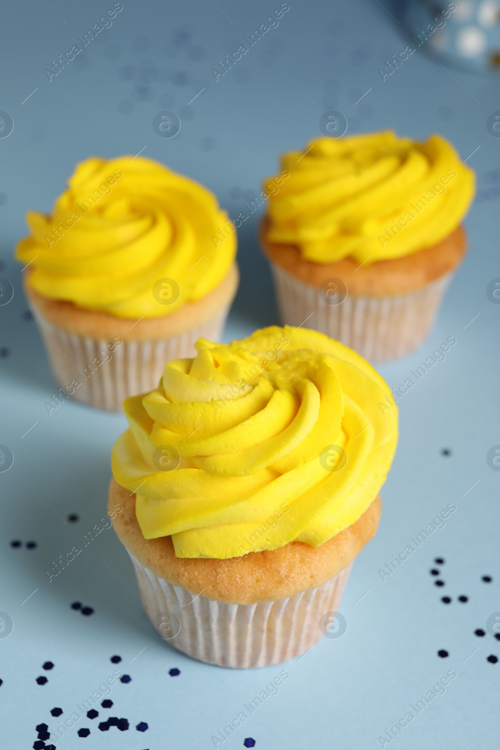 Photo of Delicious cupcakes with bright cream and confetti on light blue background, closeup