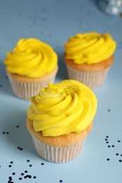 Photo of Delicious cupcakes with bright cream and confetti on light blue background, closeup