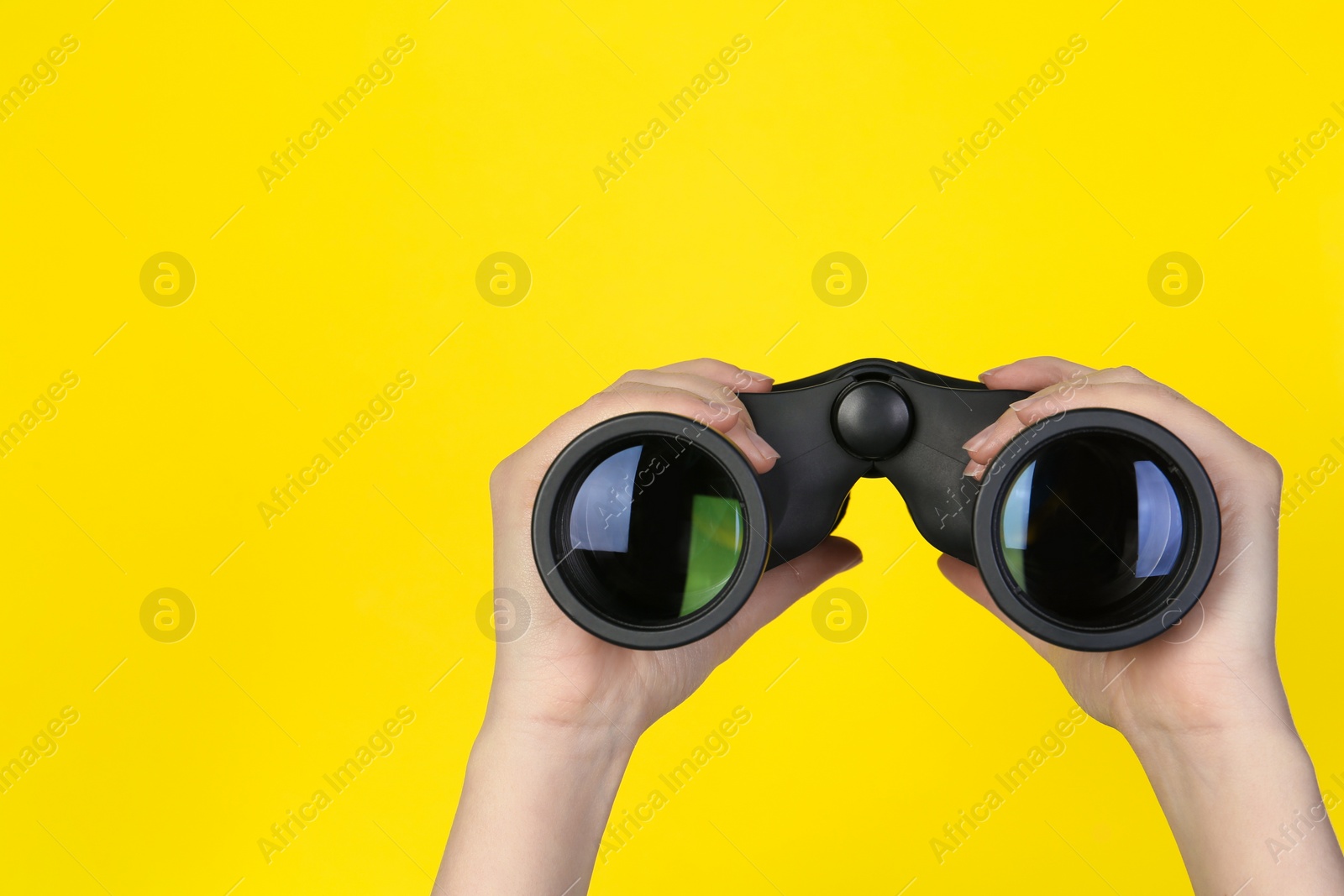 Photo of Woman holding modern binoculars on yellow background, closeup. Space for text