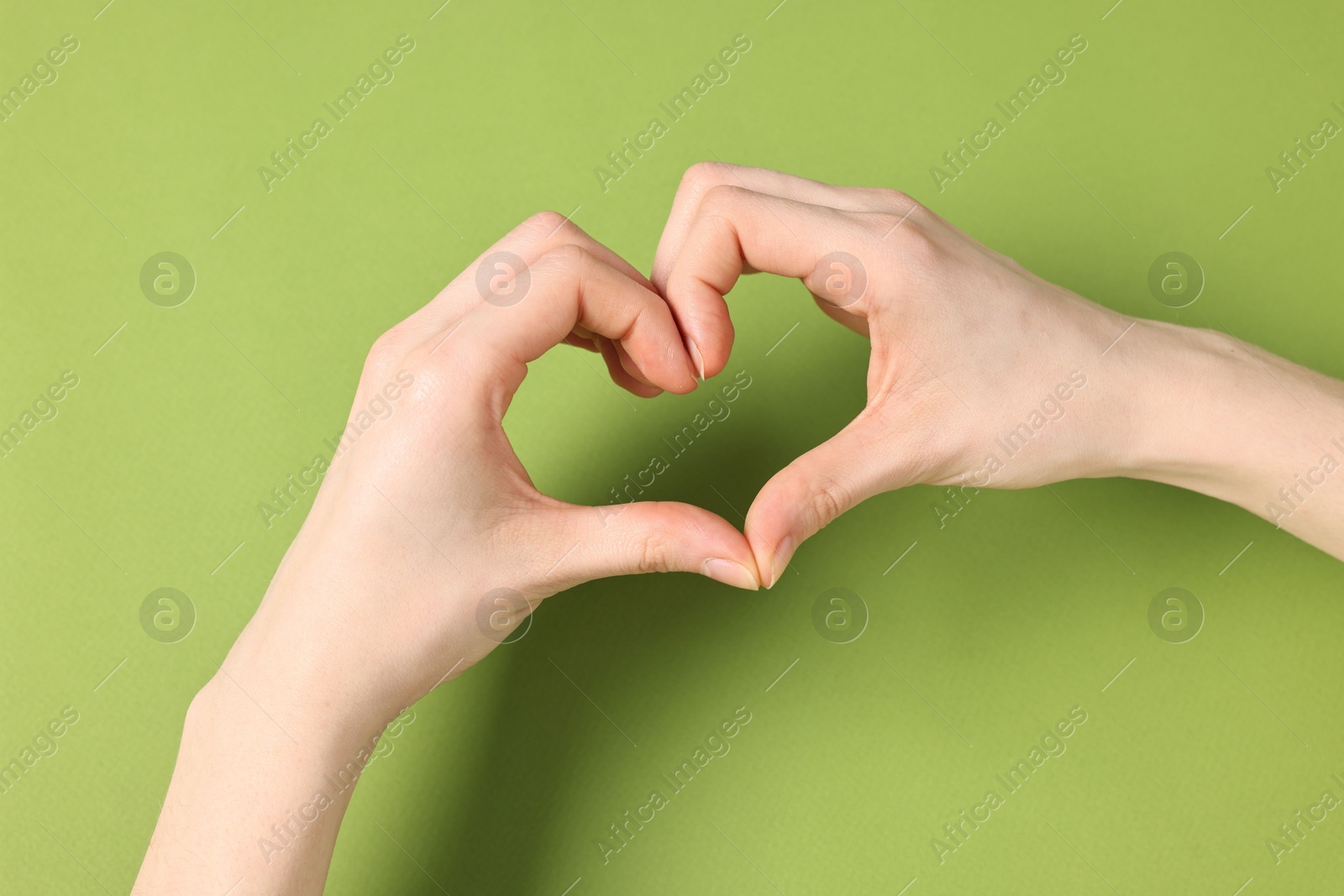 Photo of Woman showing heart gesture with hands on green background, closeup