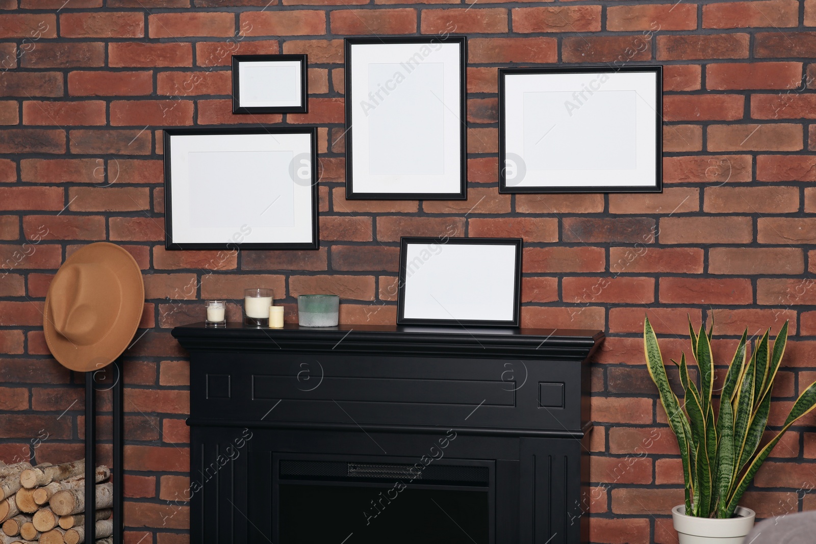 Photo of Empty frames hanging on brick wall, fireplace and potted plant candles indoors