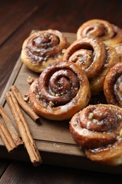 Photo of Tasty cinnamon rolls, sticks and nuts on wooden table