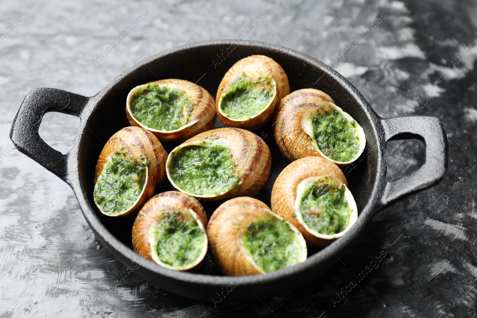 Photo of Delicious cooked snails in baking dish on grey textured table, closeup