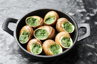 Photo of Delicious cooked snails in baking dish on grey textured table, closeup