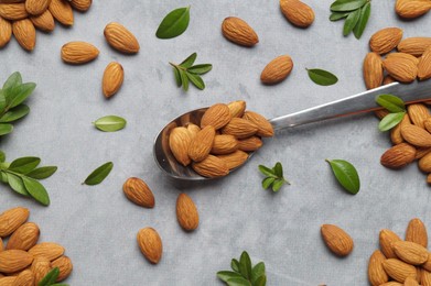 Spoon with tasty almonds and fresh green leaves on light grey table, flat lay