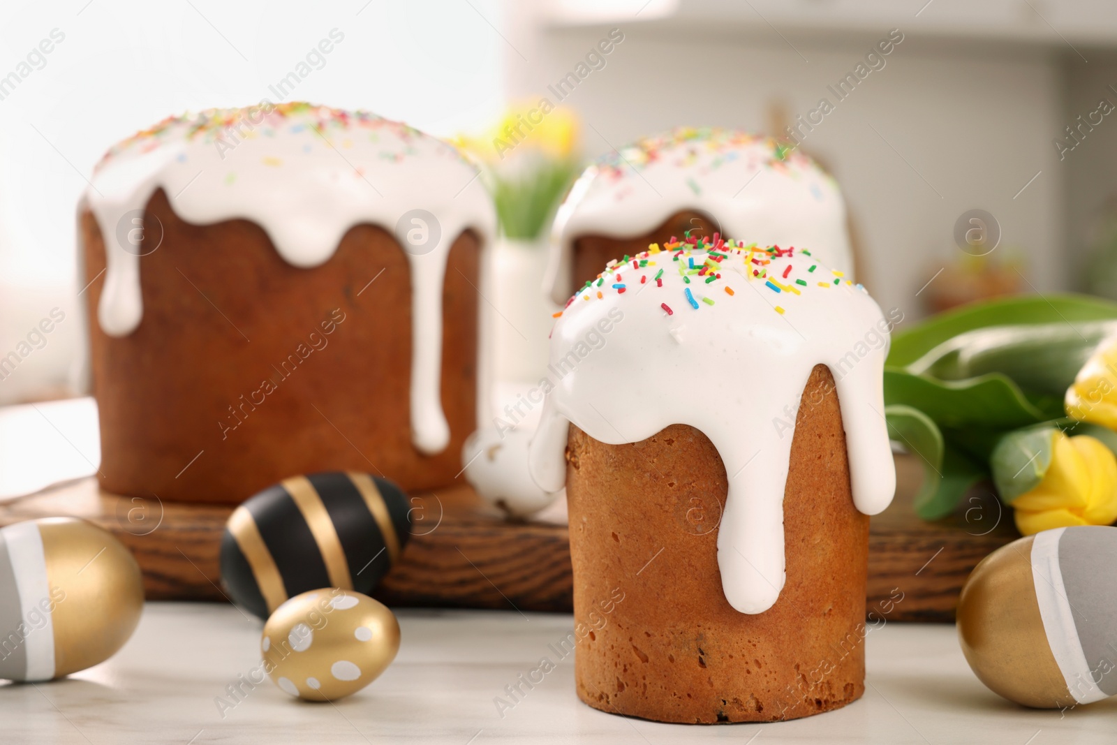 Photo of Delicious Easter cakes with sprinkles and painted eggs on white table in kitchen. Space for text