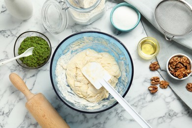 Making delicious pesto bread. Raw dough and ingredients on white marble table, flat lay