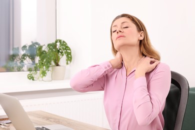 Woman suffering from pain in shoulders at wooden table indoors. Arthritis symptoms