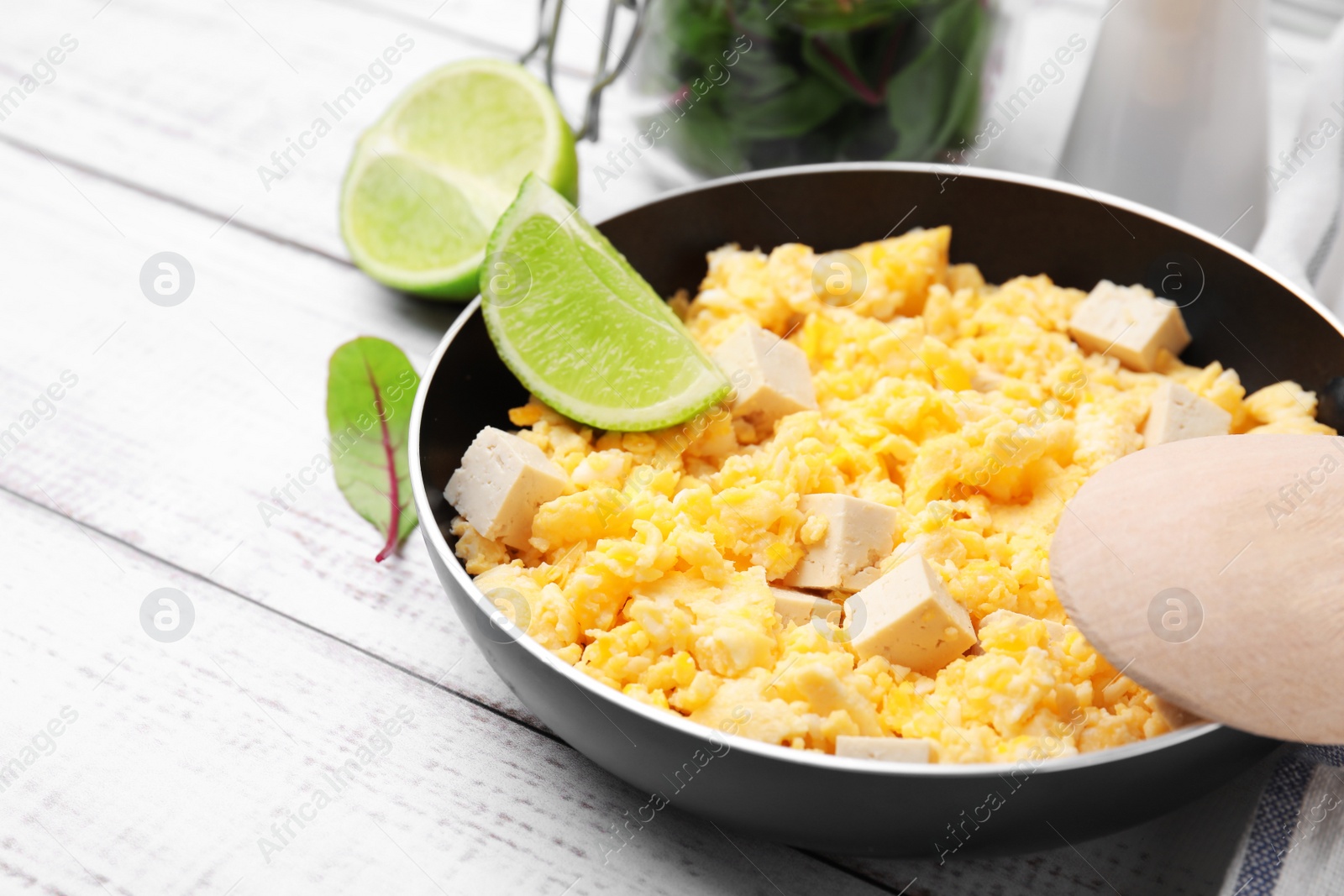 Photo of Frying pan with delicious scrambled eggs, tofu and lime on white wooden table, closeup. Space for text