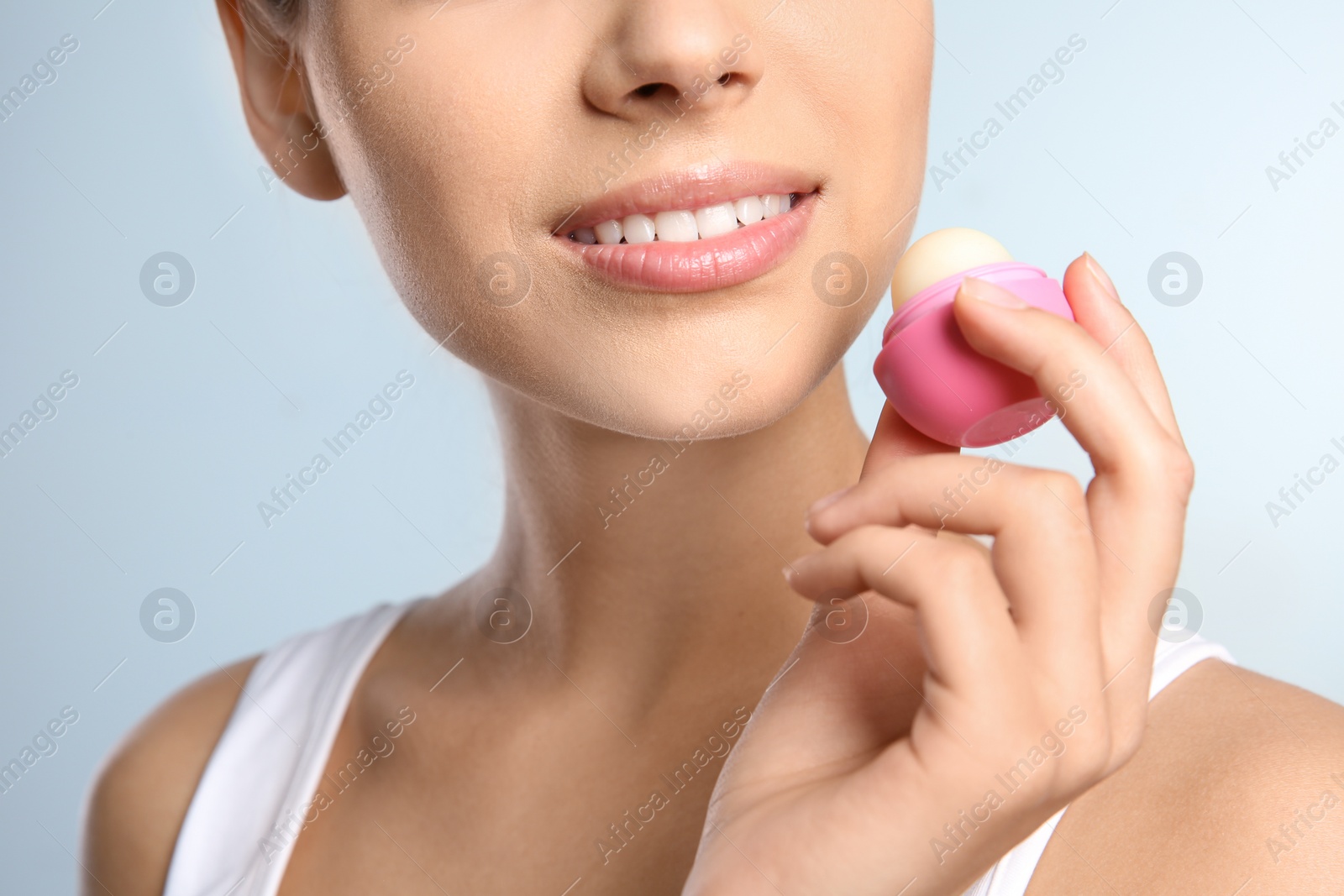 Photo of Young woman applying balm on her lips against color background, closeup