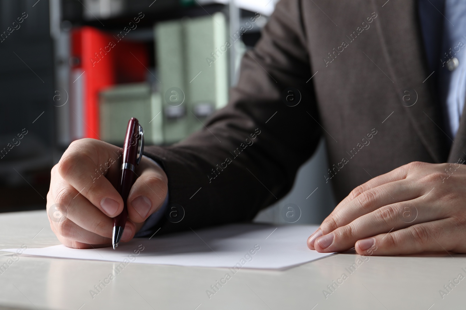 Photo of Man writing on sheet of paper with pen at white wooden table indoors, closeup