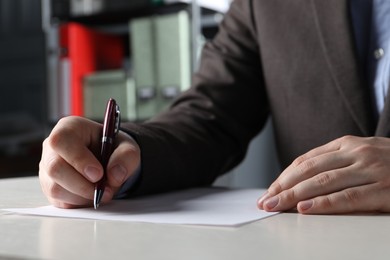 Photo of Man writing on sheet of paper with pen at white wooden table indoors, closeup